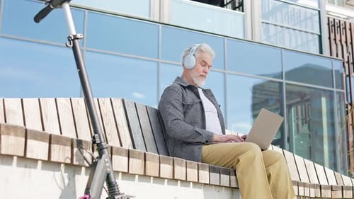 Aged Man Wearing Wireless Headset and Doing Tasks on Laptop