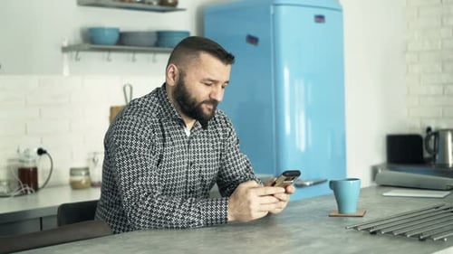 Man Uses Smartphone in Kitchen with Retro Refrigerator