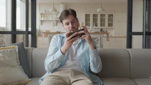 Enthusiastic Young Adult Playing Mobile Game on Couch
