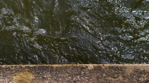 Dark Water Ripples Flowing Near a Stone Edge