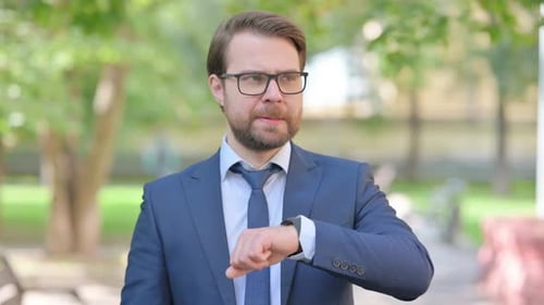Man in Suit Looks at Watch Outdoors