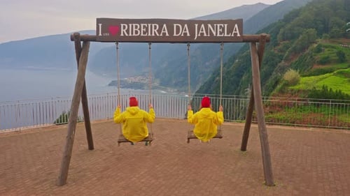 People Enjoying Coastal View on Wooden Swings