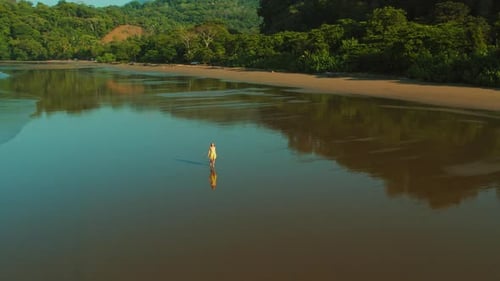 Young woman walks on mirror like sand at Playa Hermosa during sunrise in Costa Rica