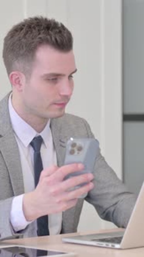 Man in Suit Using Phone and Laptop at Desk