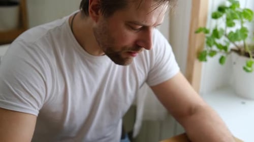 Handsome Bearded Man is Eating Green Fresh Vegan Salad in the Kitchen at Home Male Sitting at Table