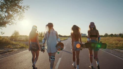 Women Skaters Walk Along Sunset Lit Road Carrying Surfskates