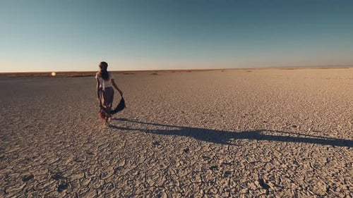 woman walking on cracked ground of dried lake. woman then starts running. sunny day. 4K.
