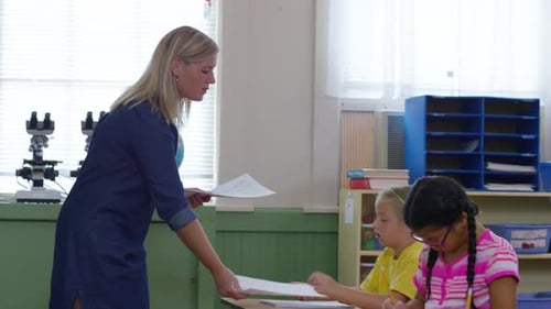 Teacher Passing Out Papers in School Classroom Child