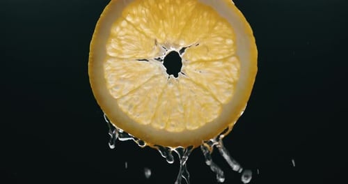 Wasser fließt in Zeitlupe über frische Orangenscheiben mit Hintergrundbeleuchtung auf schwarzem Hintergrund. Gesunder Vegetarier