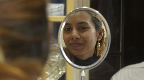 Woman Puts on Gold Earring in Mirror