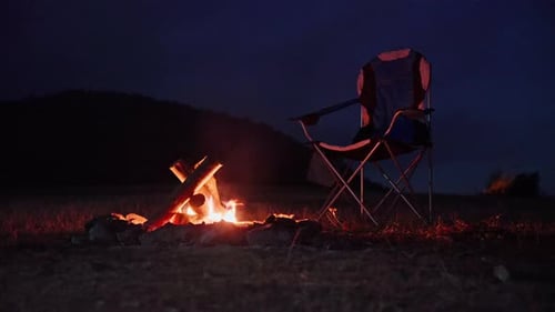 Campfire Burning Next to Folding Camp Chair at Night