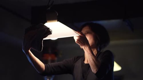 Woman Cleaning Light Fixture With Tan Cloth