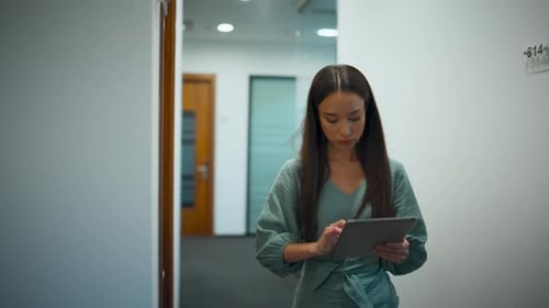 Serious businesswoman browsing internet on tablet computer in modern office hallway