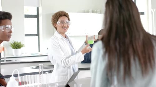 In high school, students in science lab listening to teacher holding beaker