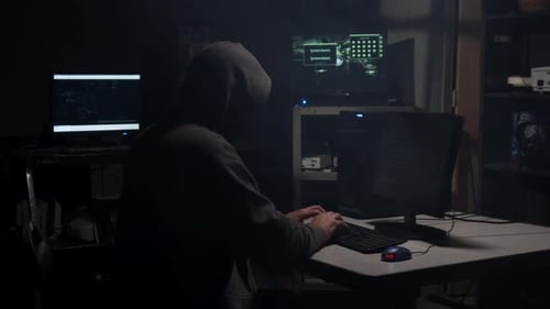 Hooded Figure Typing at Computer in Dark Room