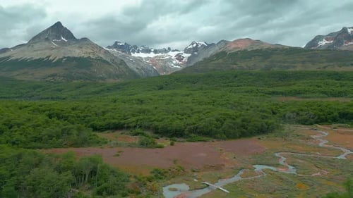 Aerial View of Ushuaia with Mountains Lush Forests and a Winding River Under a Cloudy Sky
