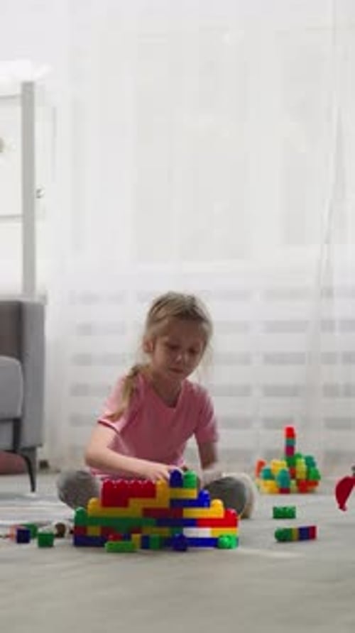 Niña construye una casa con bloques mientras un niño juega con juguetes