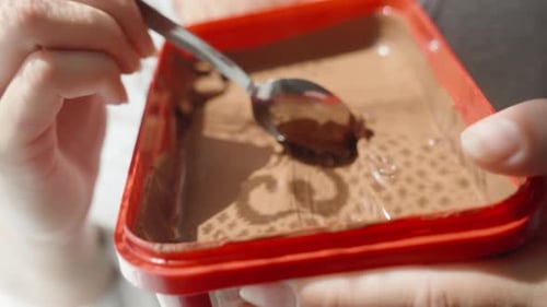 A girl eats chocolate cream from a large red jar close-up in motion.