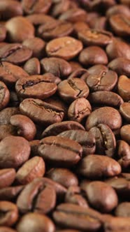 Vertical video roasted coffee beans rotating as background close-up side view. Concept for coffee