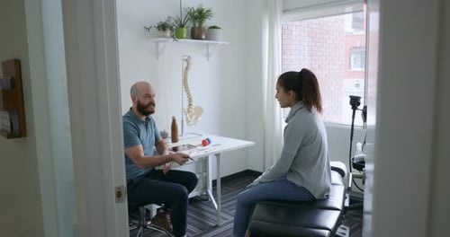 Chiropractor Talking with Woman Sitting on Examination Table