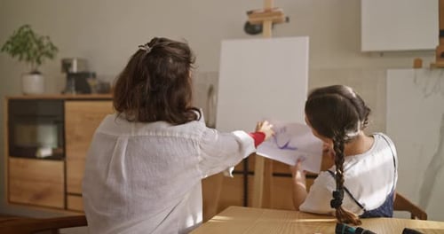 Rear View of a Brunette Woman with Her Daughter Examining Sketches of a Painting Before Starting to