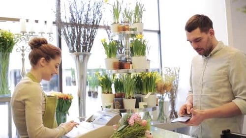 Happy florist woman counts bunch cost as man pays with credit card at flower shop
