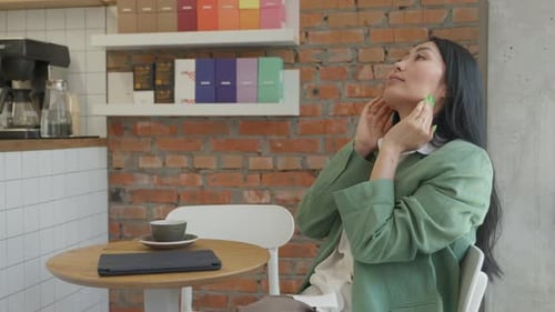Asian Businesswoman Massaging Head With Closed Eyes While Sitting In Cozy Cafe