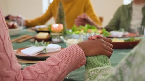 At Christmas, diverse friends holding hands around festive table, sharing gratitude and joy together
