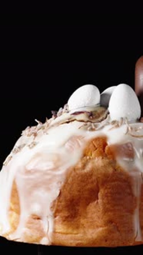 Vertical video. On a black background, a cake with white icing, a chocolate heart, and small eggs