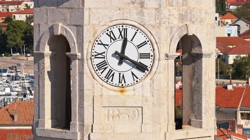 Aerial drone view of a stone clock tower featuring a large white clock face with Roman numerals and