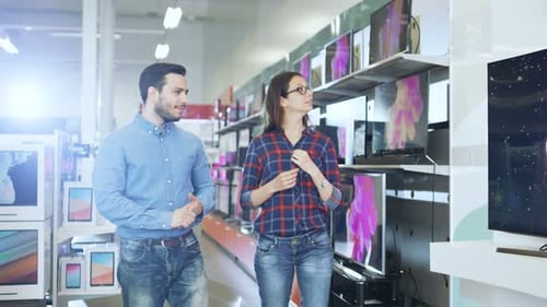 Young Couple Shopping for a New TV Set in the Electronics Store. They're Trying to Decide on the Be