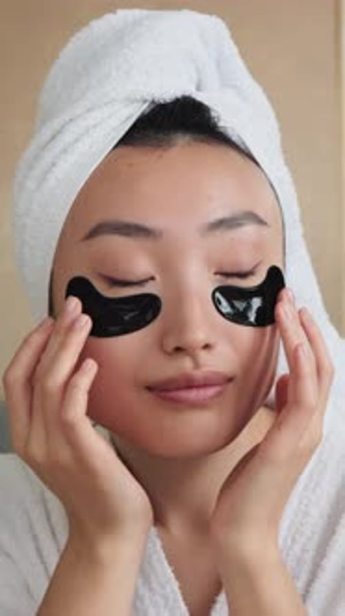 Woman applies black cosmetic eye patches in bathroom