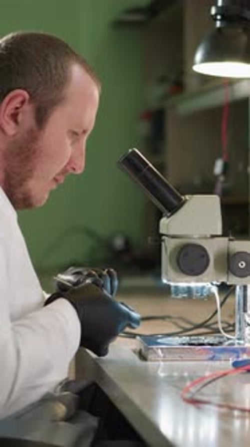 Man Examining Electronics Under Microscope in Lab