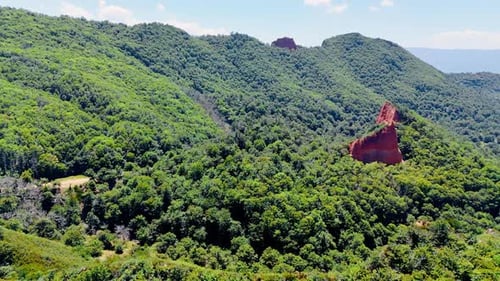 Red rock sticking out of the lush greenery covering the surrounding mountainous landscape