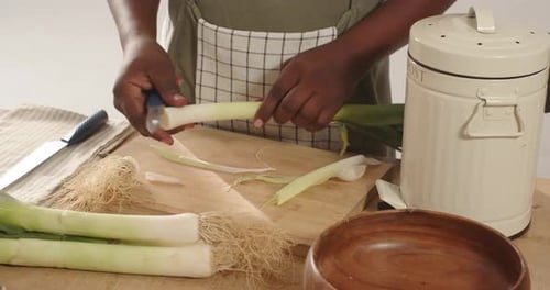 Homme afro-américain cueillant des poireaux, coupant des racines, tranchant avec un couteau sur le comptoir de la cuisine pour cuisiner