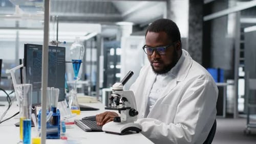 Scientist Using Microscope and Typing Data in Lab