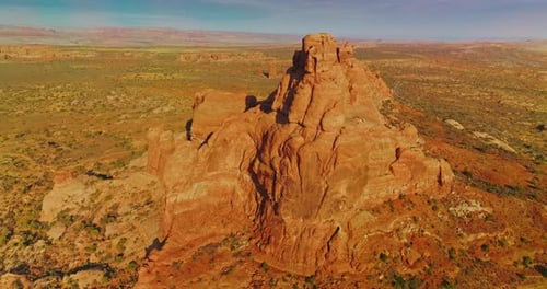 Bright sun lighting the orange mountain. Drone footage around the rock in the deserted landscape.
