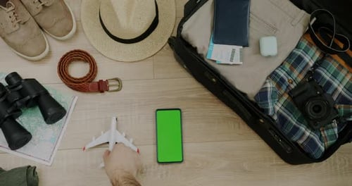 Top View of Male Hand Putting Toy Plane Next to Packed Suitcase and Travel Objects Green Screen