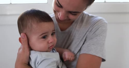 Loving hispanic mother embracing her baby boy with joyful tenderness at home