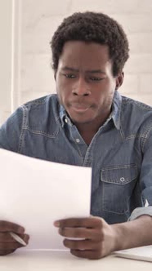 Young Man Reads Documents at Desk in Office