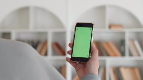Closeup of a Hand Holding a Smartphone with a Mockup Green Screen Back View with the Background of