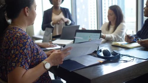 Businesswomen Discussing Paperwork at Laptops in Office Meeting 4044 Years