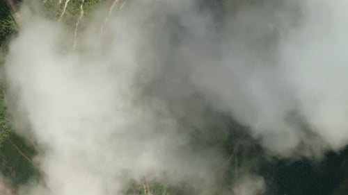Aerial tilt down view on a mountain bike trail through layer of clouds. Fluffy white clouds are movi