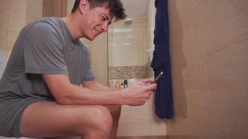 Man Sitting on Toilet Uses Mobile Phone
