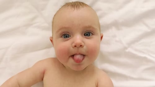 Delightful Infant Sticking Out Tongue on White Blanket