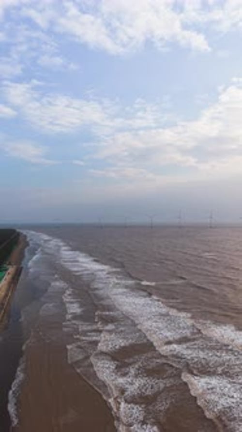 Explore the coastline of Tra Vinh, Vietnam, with waves rolling in and wind turbines in the