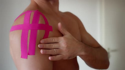 Adult Man Examines Shoulder with Kinesiology Tape