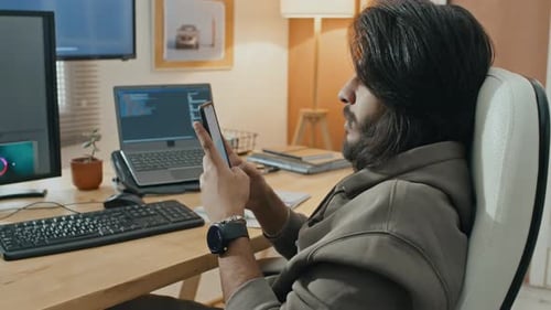 Jeune programmeur tapant sur un smartphone tout en travaillant à domicile