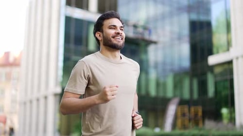 Young adult male runner jogging along a park alley on a city street. Handsome active man in a t-shir
