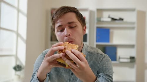 Portrait of man eating burger in office at lunchtime